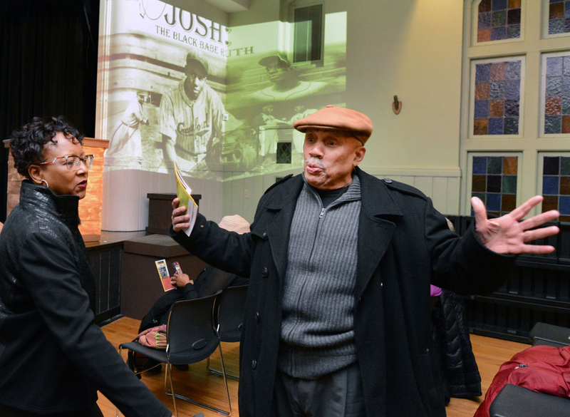 Ronald Saunders, a retired civil rights activist, speaks with Kim Lester of Clairton, Pa., before the start of the New Horizon Theater’s presentation of “Josh: The Black Babe Ruth.” Saunders volunteers with the theater, greeting patrons and handing out programs. (Nate Guidry/Pittsburgh Post-Gazette)